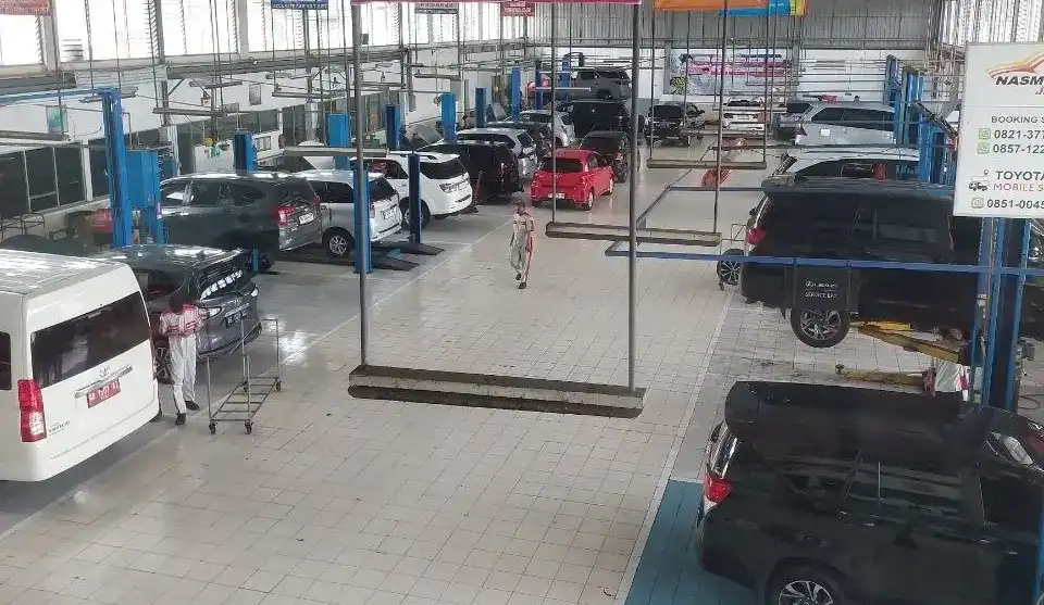 Auto repair shop with multiple cars on lifts and technicians walking between vehicles indoors.