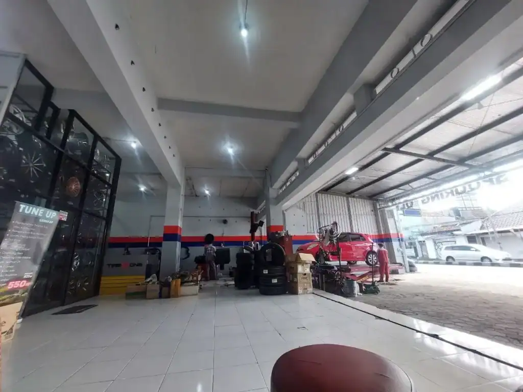 Auto repair shop interior with stacked tires, tools, and a red car on a lift near the storefront entrance.